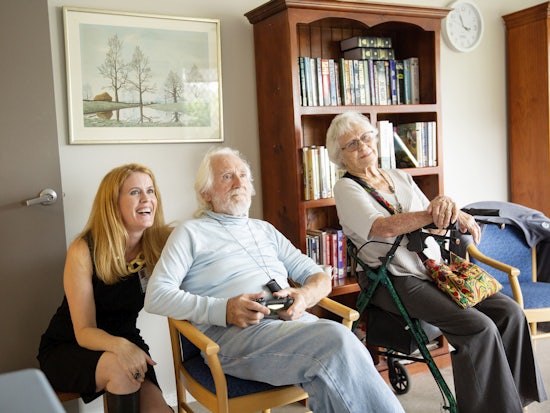 <p>Psychology and Behavioural Science Researcher from the University of England, Alex McCord, with Feros Village residents, Hugh Webster and Lois Sanderson, playing video games. [Source: Feros Care]</p>

