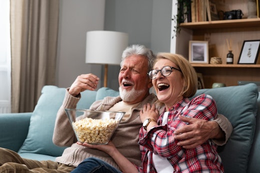 Old man and old woman together on couch, eating popcorn