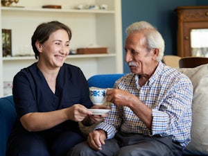 Older man receiving a cup of tea from a home care worker