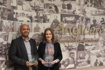 Two award recipients stand in front of a wall reading Anglicare