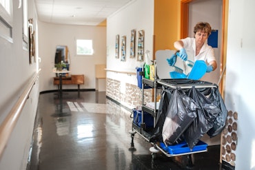 A cleaner in an aged care home hallway with her cart