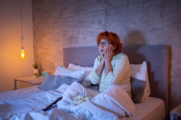 An older woman sits up in bed.