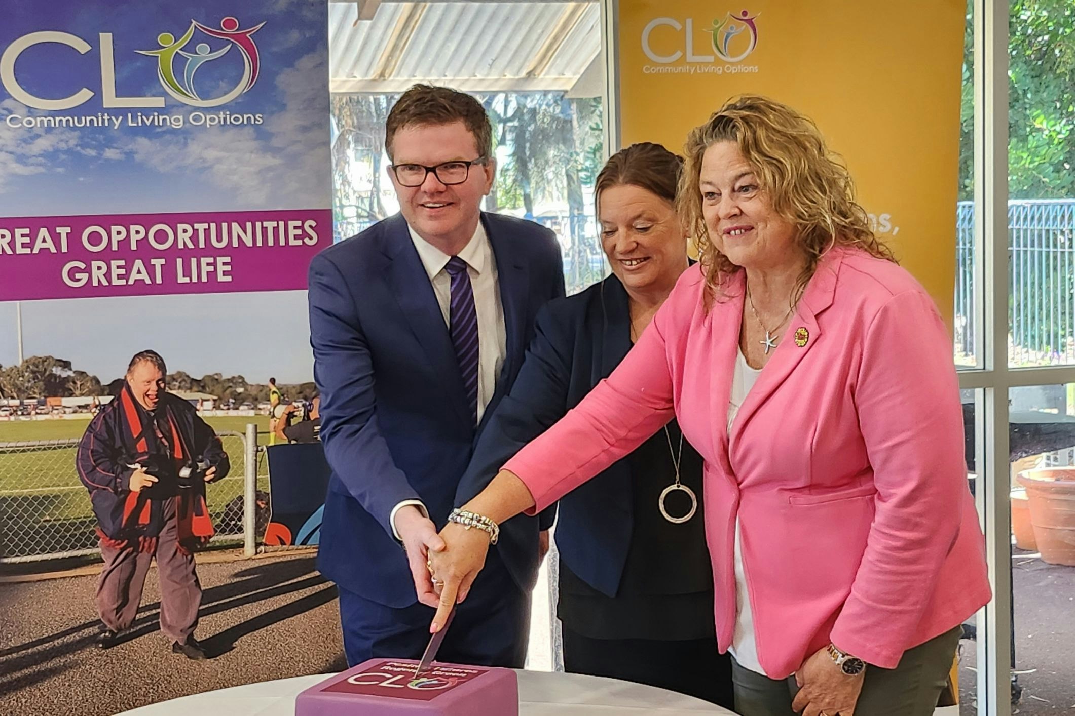 Minister for Health and Well-being Chirs Picton MP [left], Minister for Human Services Nat Cook MP [right] and Community Living Options CEO Mel Kubisa [centre] cut the commemorative cake on Friday morning. [Source: Disability Support Guide]
