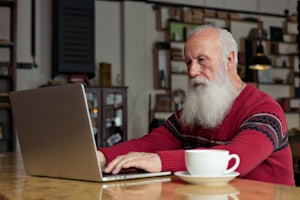 An older gentleman sits at home with a laptop.