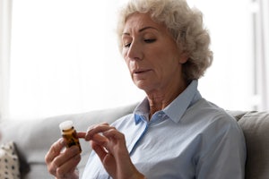 Older woman looks at pill bottle.