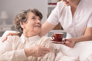 Older woman accepting tea from a carer at her home.