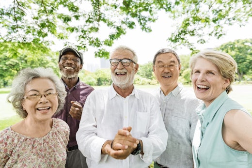 A group of older people stand in front of a green background.