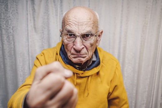 An older man wearing a yellow jumper holds his fist up.