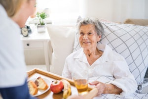 An aged care worker brings breakfast to a woman in bed