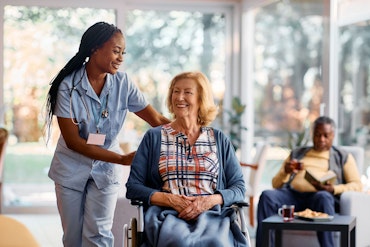 A woman pushes a woman in a wheelchair in an aged care home