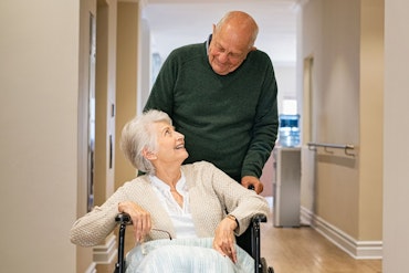 An older man looks at an old woman in a wheelchair