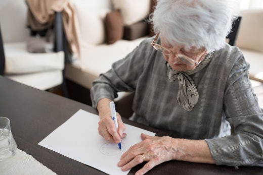 An older woman draws a clock on a piece of paper