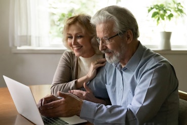 An older man and woman look at a computer together