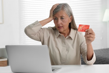 An older woman looks worried as she holds her head and a credit card