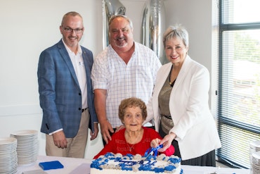 Four people stand behind a cake and cut it