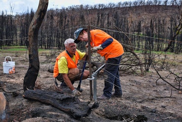 Two people repair a fence after a fire