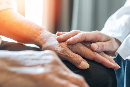 A doctor rests their hands on an older person's hands