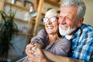 An older man hugs an older woman from behind