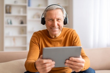 A man looks down at a tablet while wearing earphones.