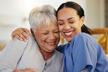 An older woman is hugged by a younger aged care worker