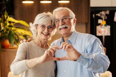 Two older people make a heart shape with their hands