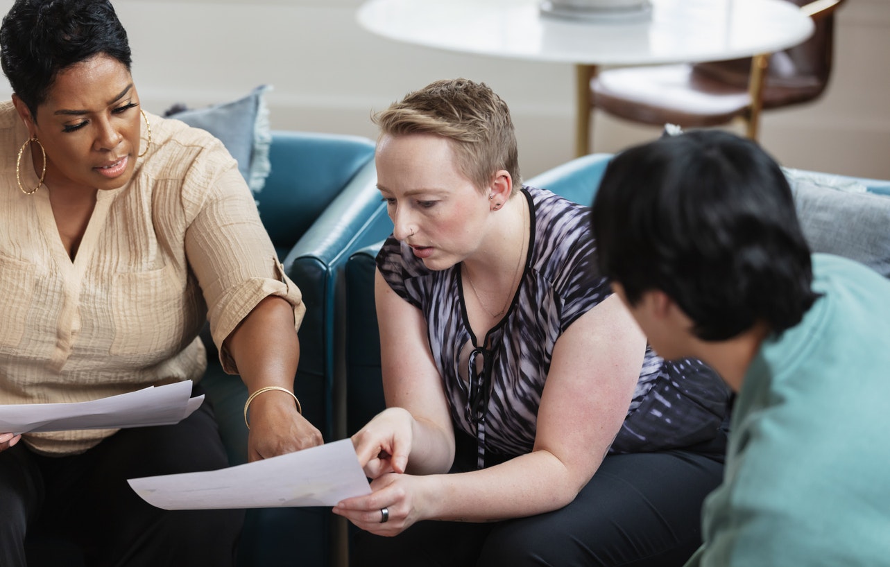 <p>A multiracial group of three people meeting together in the lounge area of a coworking office space. </p>
