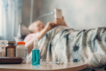 Older woman in aged care looks at phone, with in-focus shot of bedside table and medicines