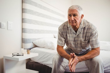 A man sits on a bed and looks worried