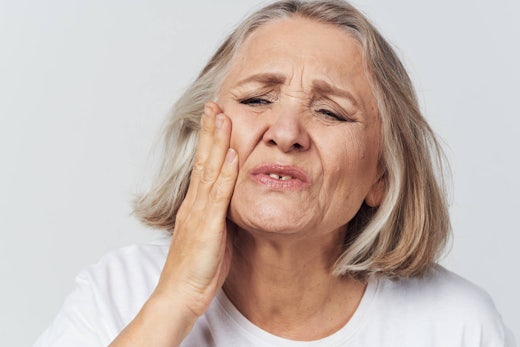 Older woman clutches side of her mouth in pain