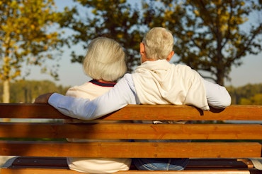 An older couple's back face the camera as they sit on a bench