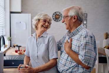 Two older people smile at each other in a kitchen