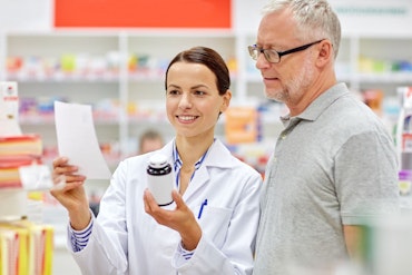 A pharmacist holds a bottle while talking to a customer.