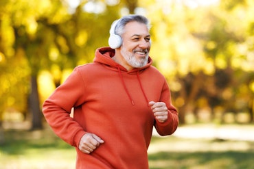 An older man in a red jumper is running in a park