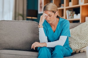 A nurse holds her head as she sits on a sofa