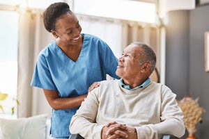 A woman in scrubs smiles at an older man who is sitting