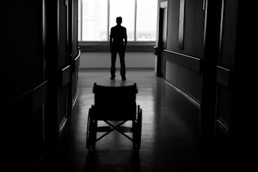 A silhouette of a person and a wheelchair in a hallway.