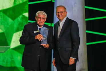 Two men stand in front of a green background