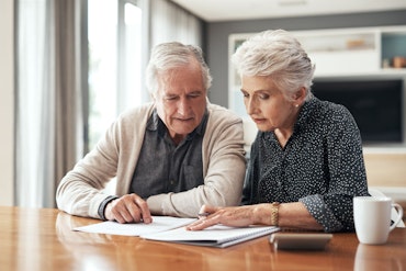 An older couple sit at a desk looking at papers.