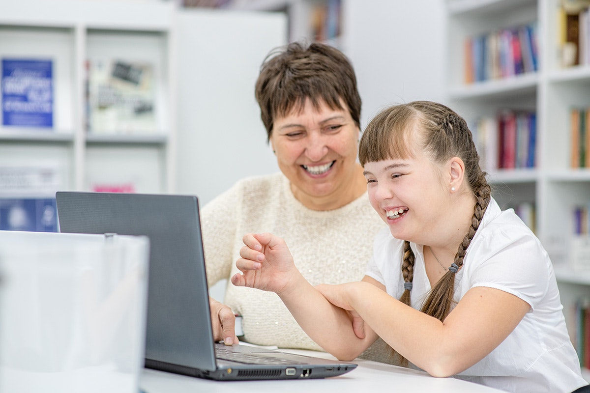 Lady helping girl on laptop [Source: Shutterstock]