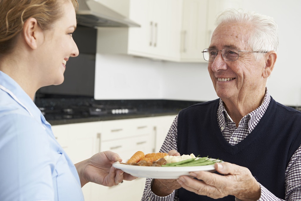 Older man receiving help making his dinner from a carer