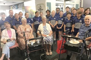 A group of students stand behind residents of an aged care home