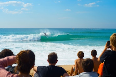 A crowd watches as a surfer rides the waves.