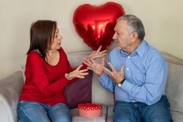 Two older people argue in front of a balloon heart