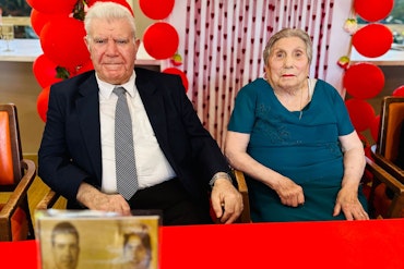 A couple sits together in an aged care facility adorned in red Valentine's Day decor