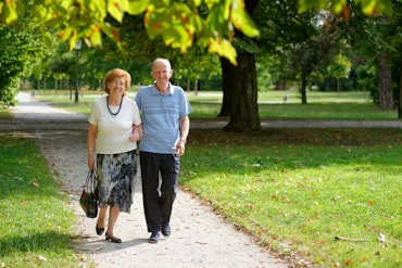 Two older people walk through a park on a path