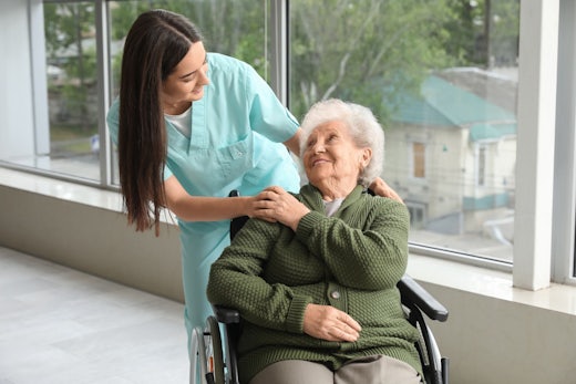 A nurse places her hand on the shoulder of an older woman in a wheelchair