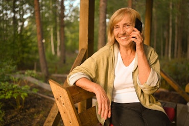 A woman holds her phone while sitting in a forest