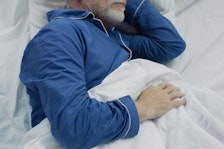 A man in blue pajamas sleeps in white sheets.