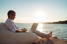 Older man sitting by the ocean on laptop
