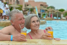 Retired couple holding cocktails by the pool.